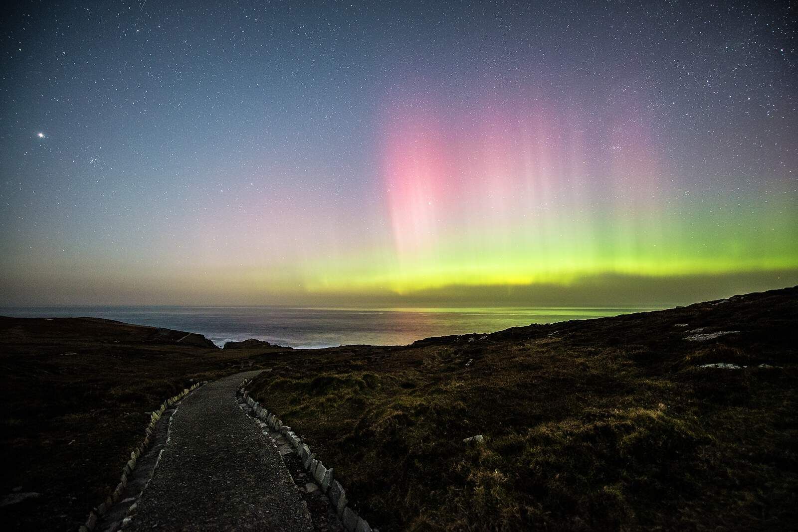 A starry night sky with the Northern Lights over a coastal landscape.