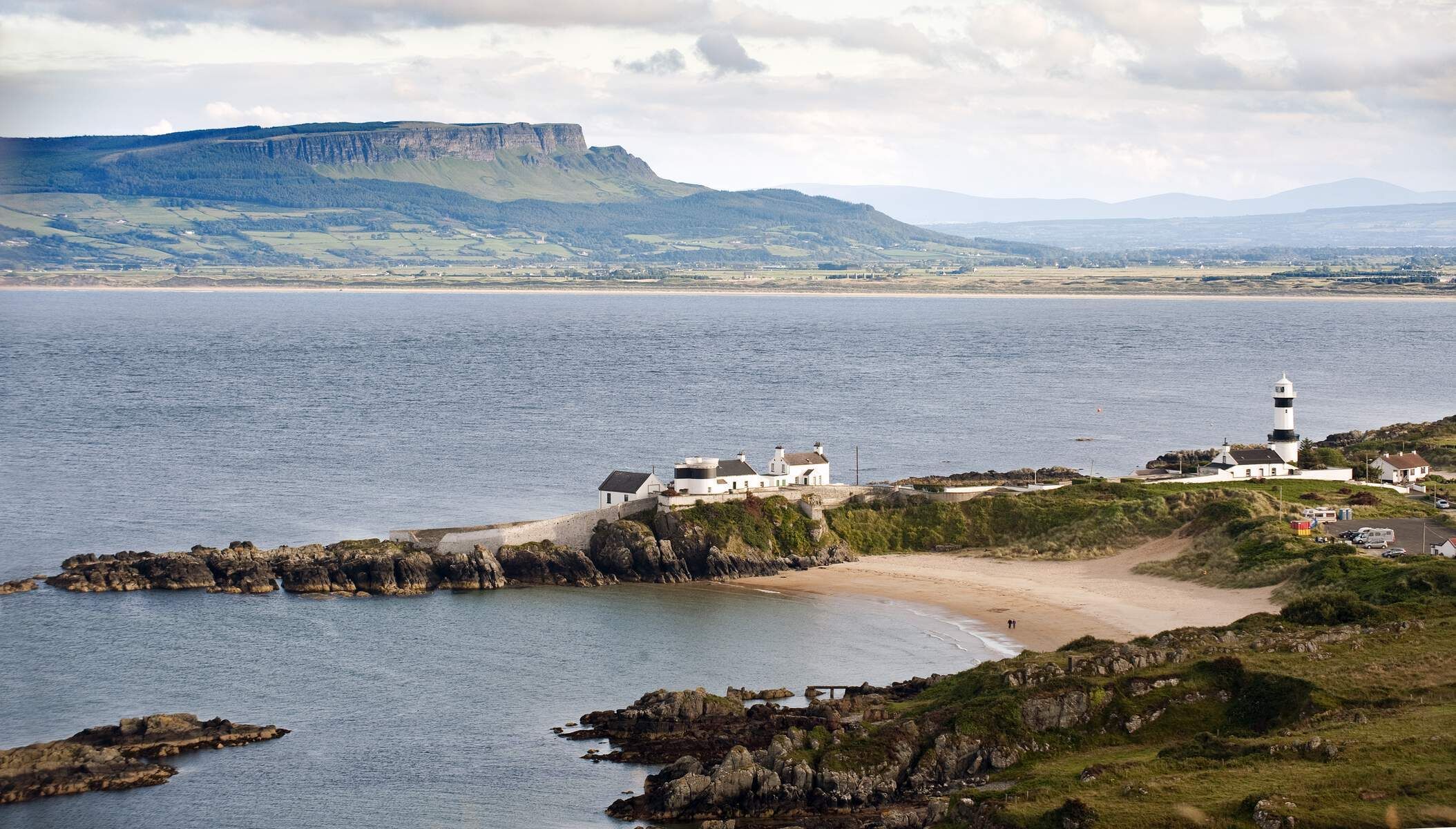 A coastal scene with a lighthouse, a large white building, and rocky terrain.