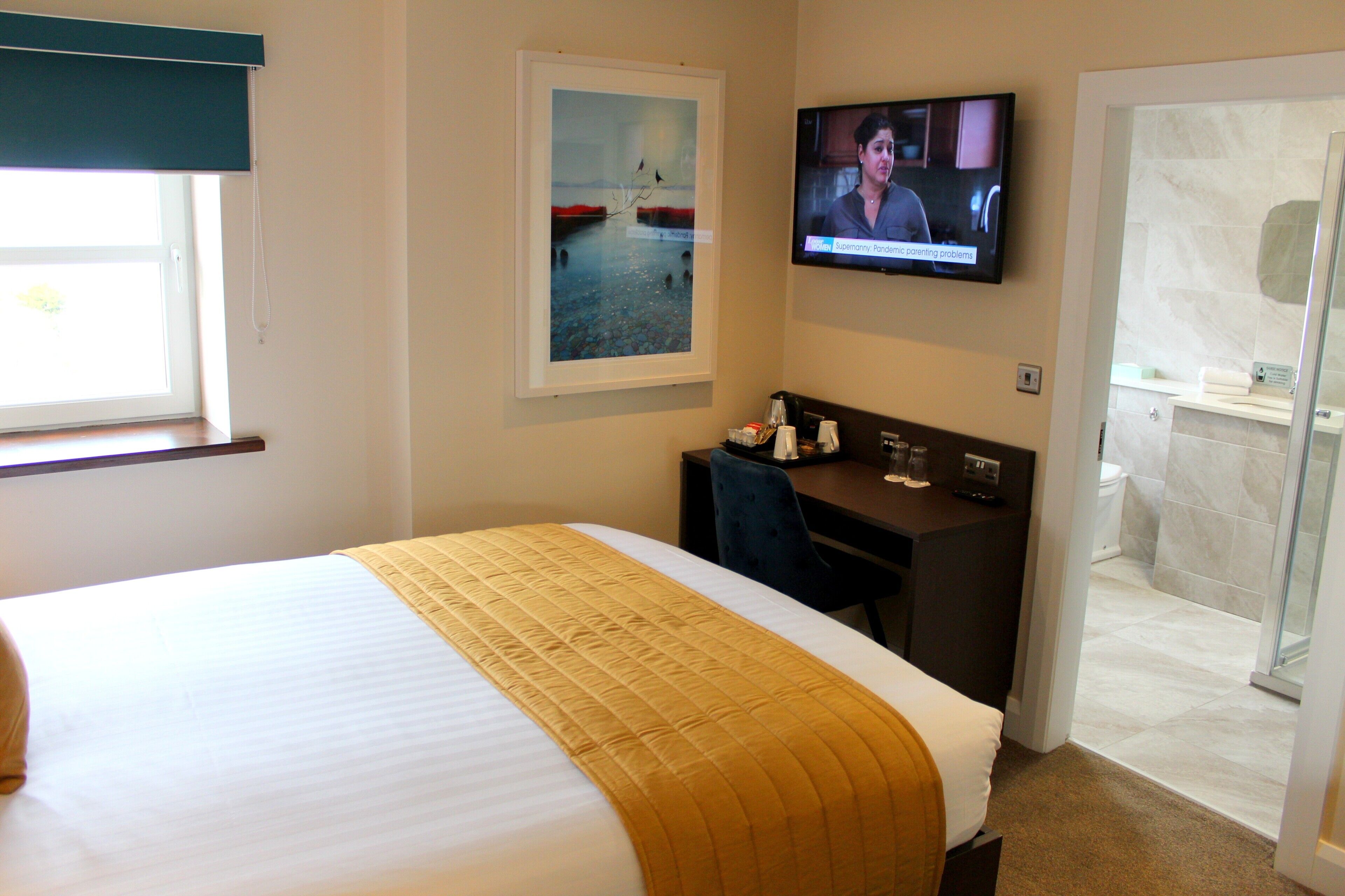Habitación de hotel con cama, escritorio, televisión y baño visible a través de una puerta abierta.