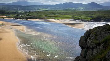 A coastal landscape with a beach, clear waters, and distant mountains.