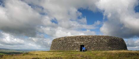 Una estructura de piedra con entrada circular, rodeada de terreno cubierto de hierba y bajo un cielo parcialmente nublado.