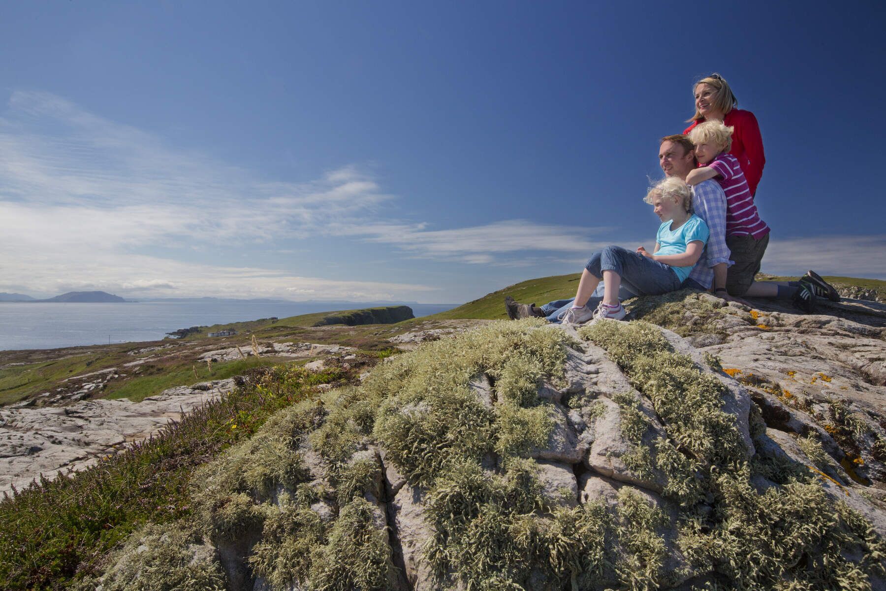 A family on a rocky outcrop with a view of the sea and distant hills.