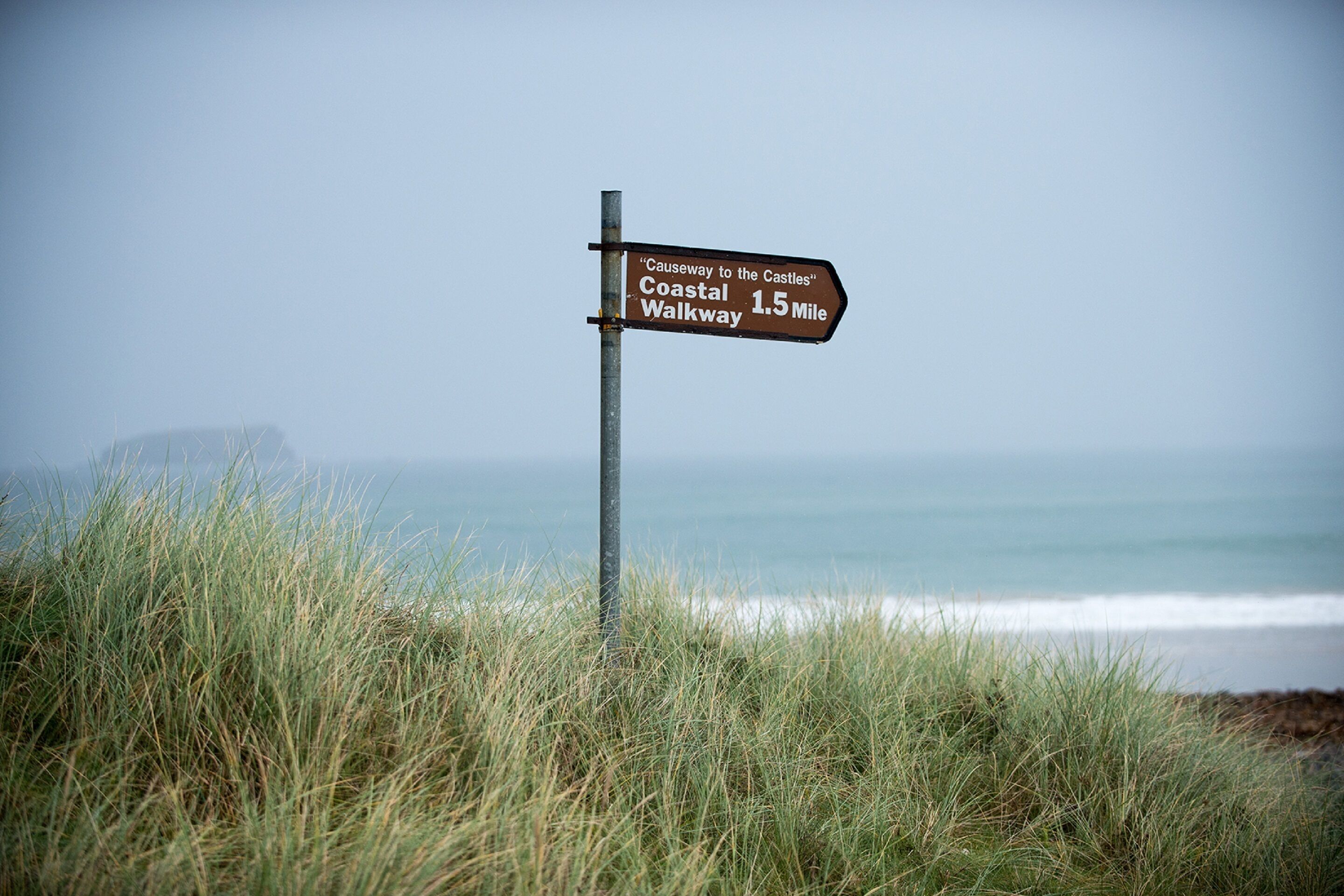 A directional signpost with "Coastal Walkway 1.5 Mile" and "Causeway to the Castles" written on it.
