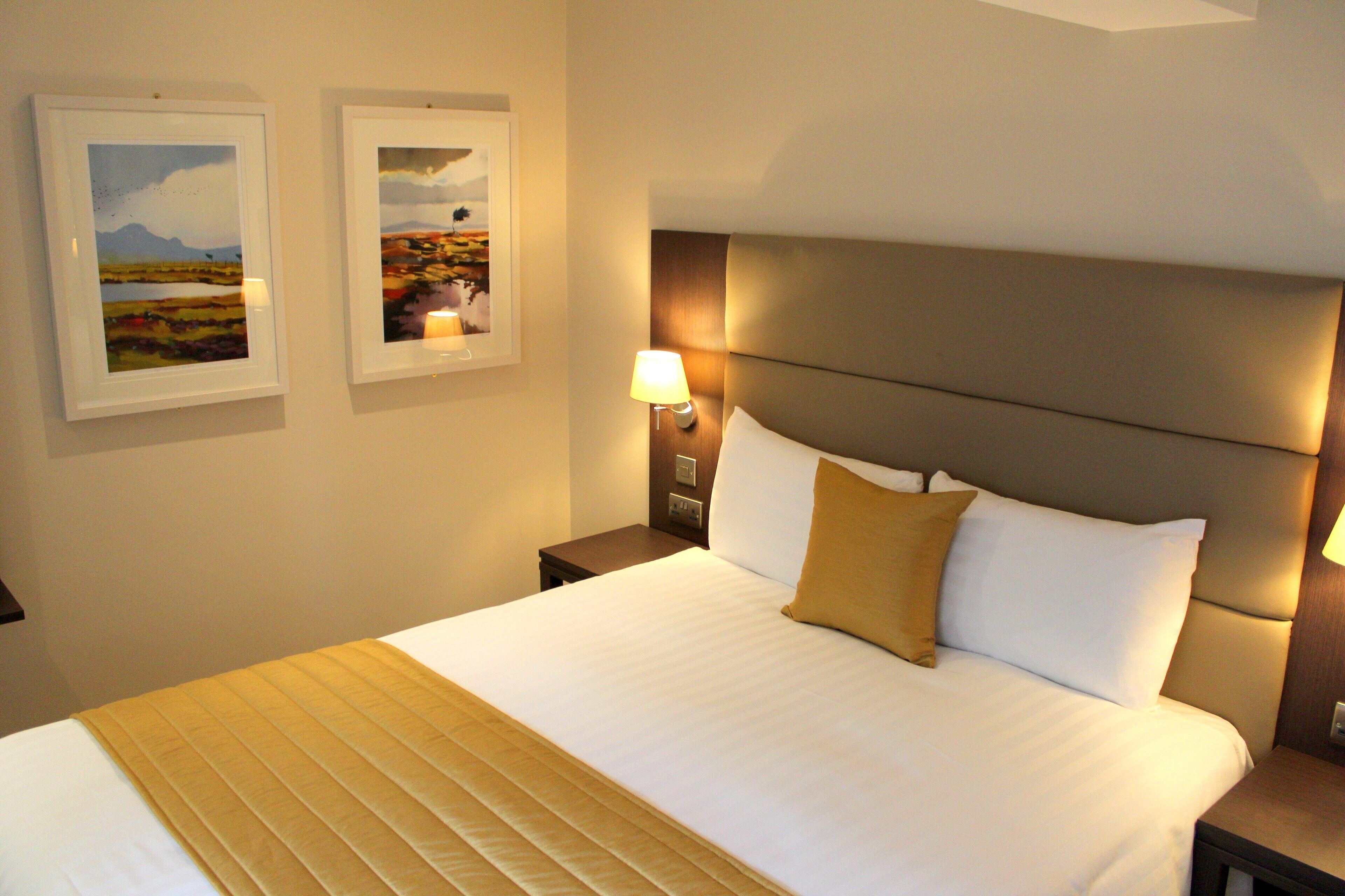 A neatly made bed with a headboard, a bedside lamp, and two framed pictures on the wall.