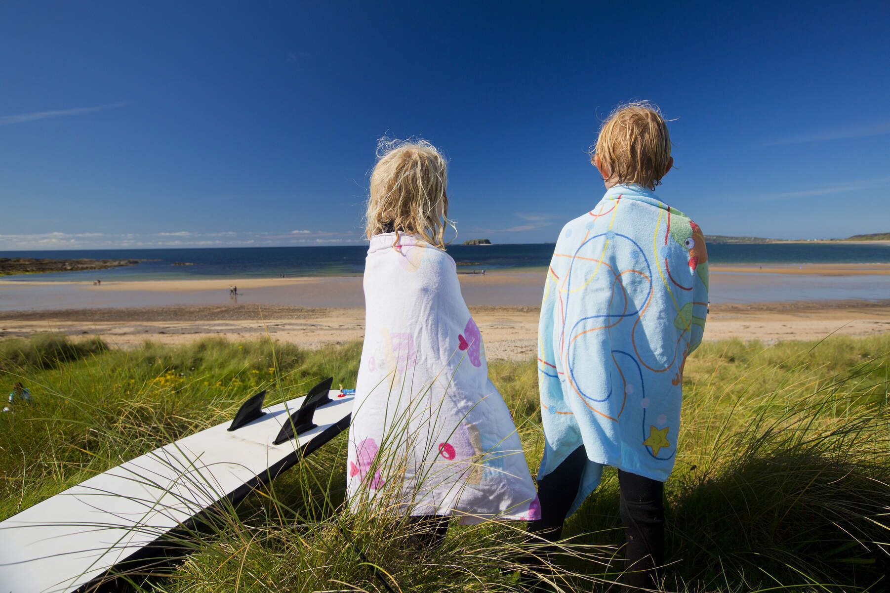 Deux personnes se tiennent debout sur une pelouse, d’où elles dominent une plage, sous un ciel dégagé.