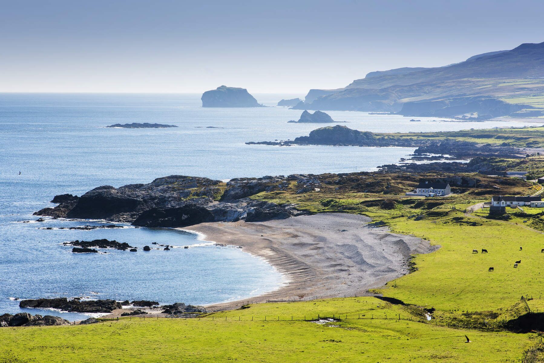 A coastal landscape with a grassy field, rocky coastline, and a house with a view of the sea.