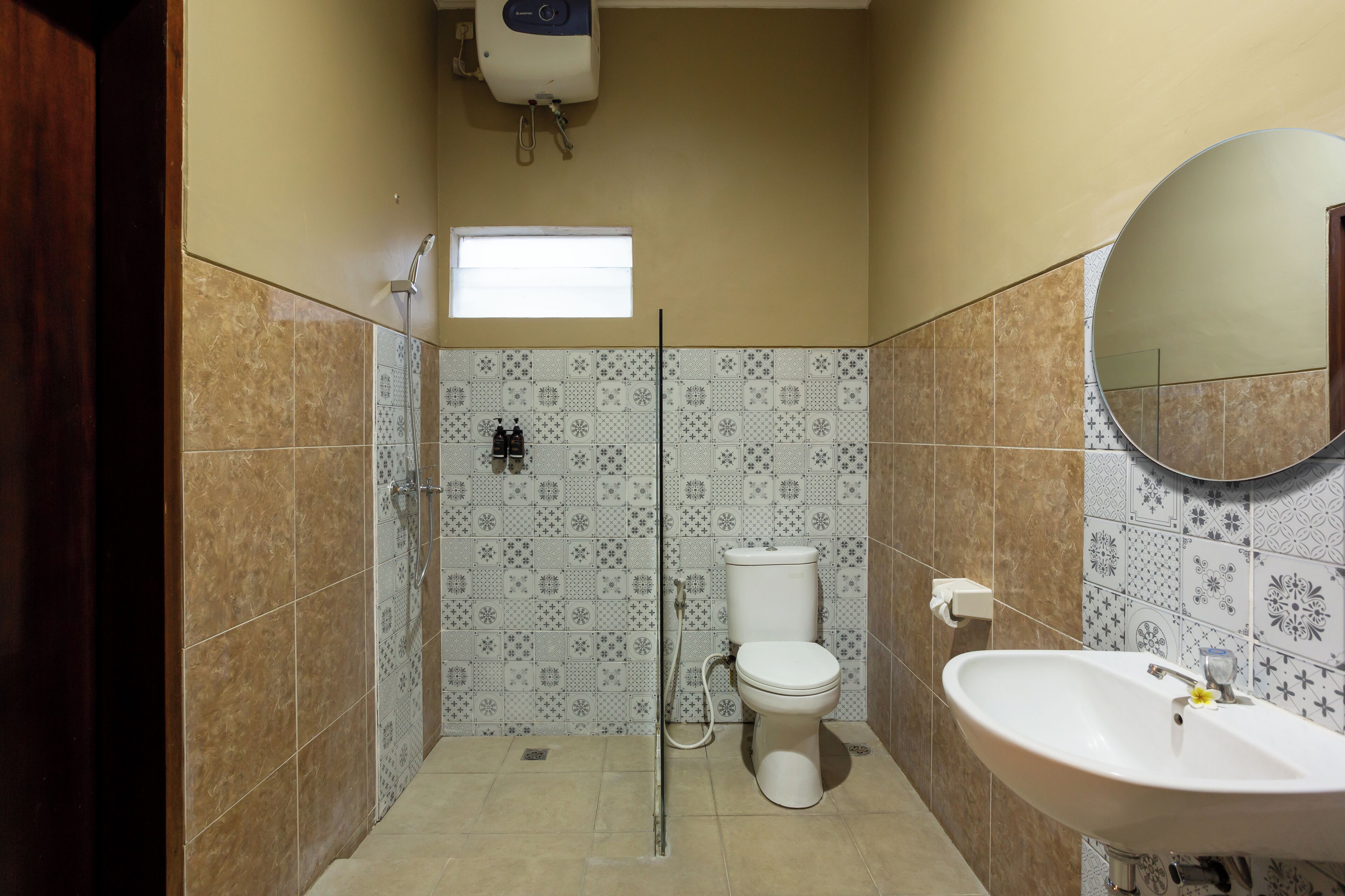 Une salle de bain équipée d’une douche, de toilettes et d’un lavabo, avec des carreaux décoratifs et un miroir.