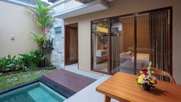 A modern outdoor area with a pool, a dining table with a flower vase, and a glass door leading to a bedroom. - Karana Villa Bali (Denpasar)