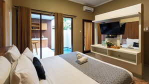 A hotel room with a bed, a TV, a desk, and a sliding door to a balcony. - Karana Villa Bali (Denpasar)