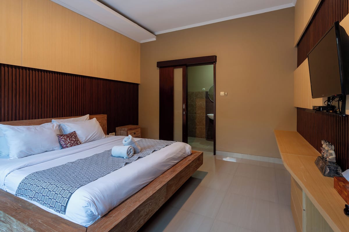 A modern bedroom with a large bed, wooden headboard, and a flat-screen TV mounted on the wall.