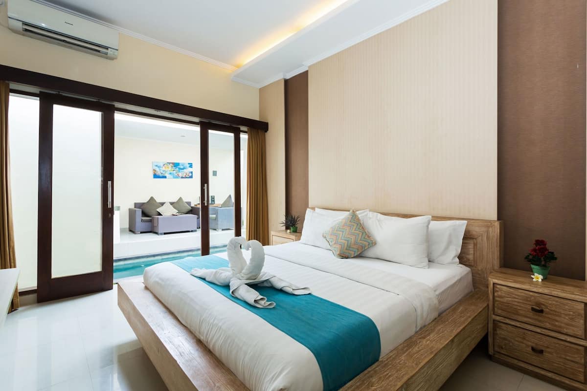 A hotel room with a bed, a nightstand, a wooden headboard, a window, and a view of the pool area.