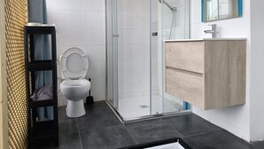 Un baño moderno con cabina de ducha de vidrio, inodoro blanco y tocador de madera con espejo.