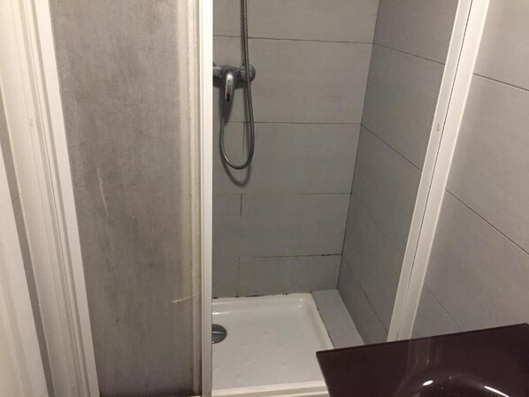 A small, enclosed shower area with a white floor and grey tiles.