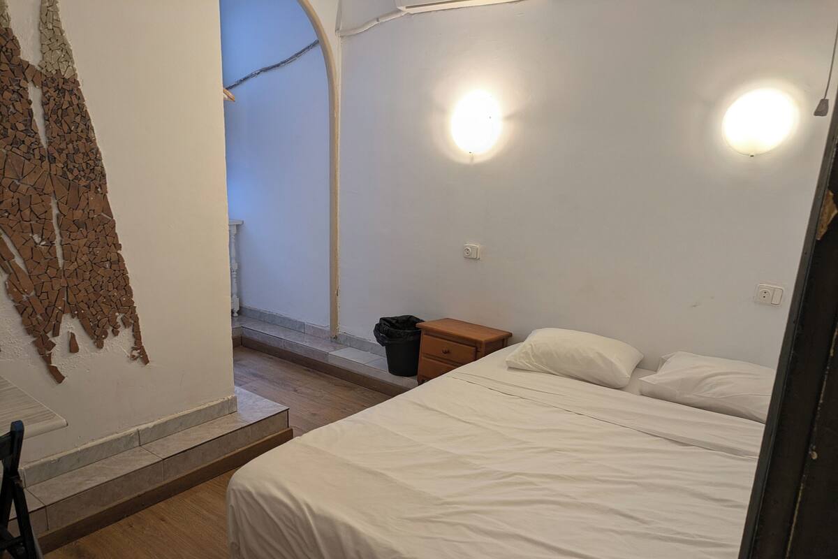 Ein Schlafzimmer mit einem Bett, einem Nachttisch, einem Mülleimer und einer Wand mit Riss.