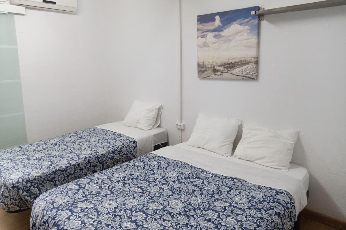 Ein Zimmer mit zwei Einzelbetten, einem Landschaftsbild und einer weißen Klimaanlage.