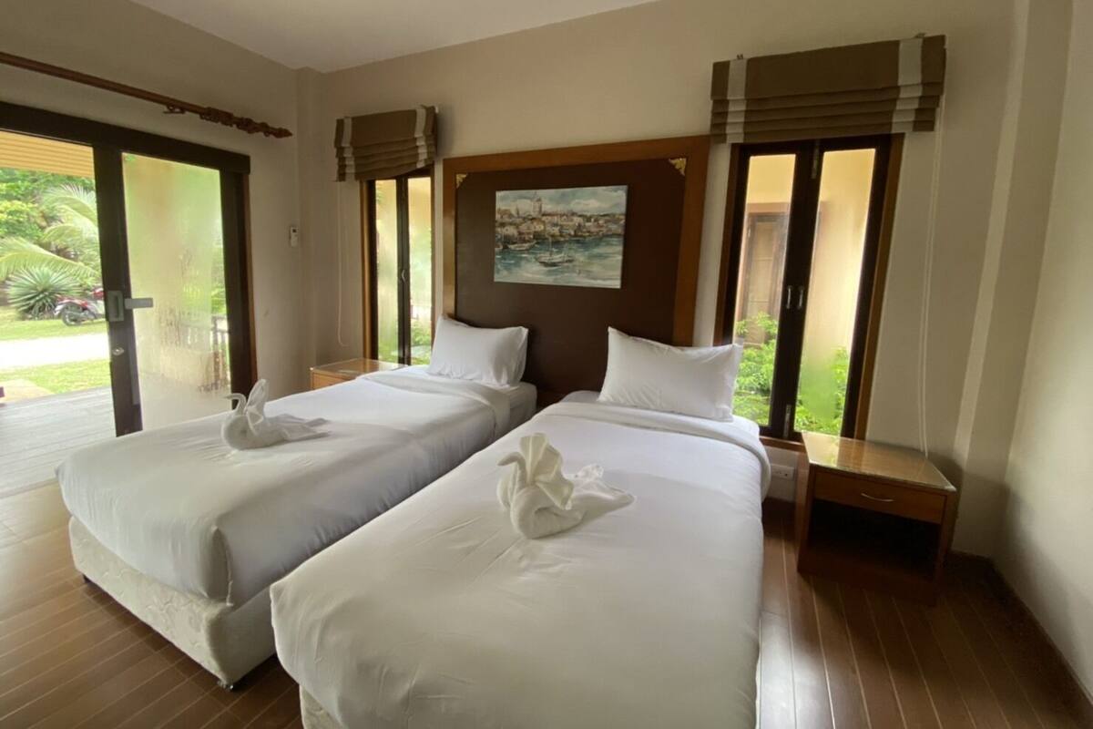 A hotel room with two beds, a painting on the wall, and a view of the outdoors through large windows.
