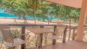 A covered outdoor seating area with a table and chairs, overlooking a beach and palm trees. - Chaithalay Khanom Resort (Khanom)