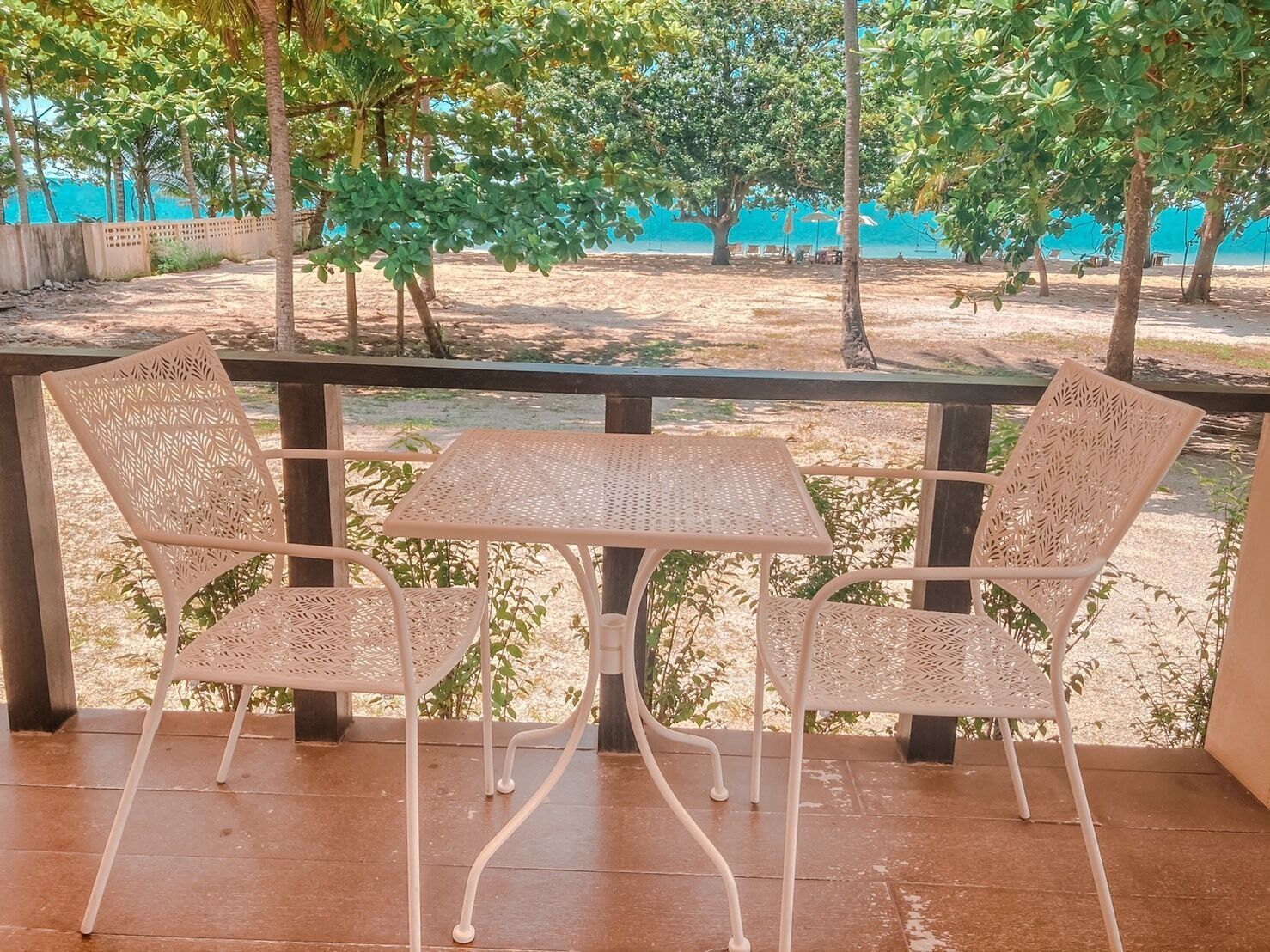 A covered outdoor seating area with a table and two chairs, overlooking a sandy beach and a blue sea.