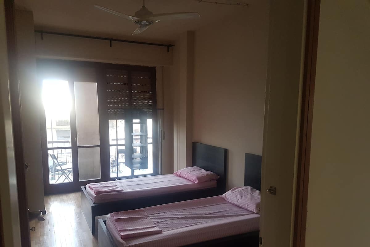 A room with two beds, a ceiling fan, and a sliding door leading to an outdoor area.