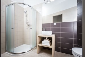 Un baño moderno con ducha de vidrio, lavamanos blanco sobre estante de madera y un inodoro.