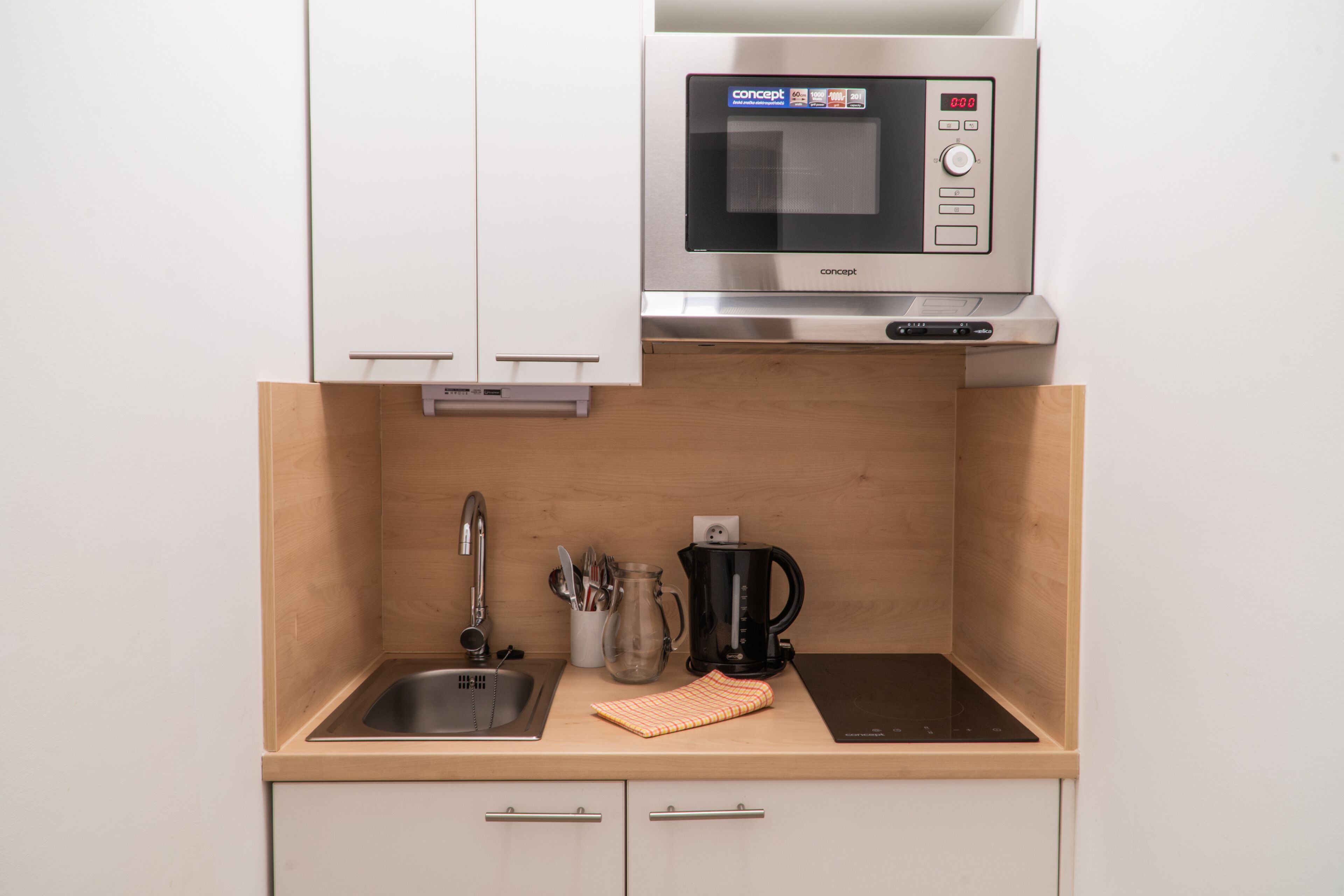 Una cocina compacta con microondas integrado, un lavamanos y una cafetera.