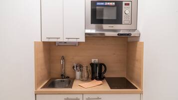 Una cocina compacta con microondas integrado, un lavamanos y una cafetera.