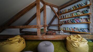 Een slaapkamer in een loft met zichtbare houten balken, een boekenkast en twee loungestoelen op een groen tapijt.