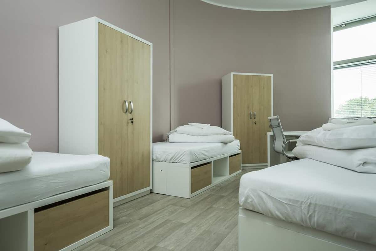 A modern bedroom with two beds, wooden wardrobes, and a desk.