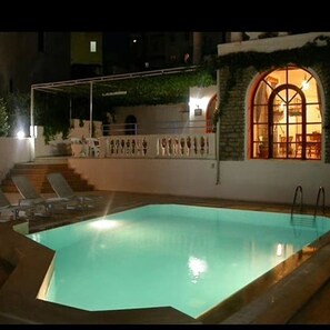A swimming pool with a stone wall and arched window. - Sahin Apart Otel (Bodrum)