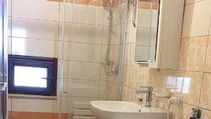 Een kleine badkamer met douche, toilet, wasmachine en wastafel.