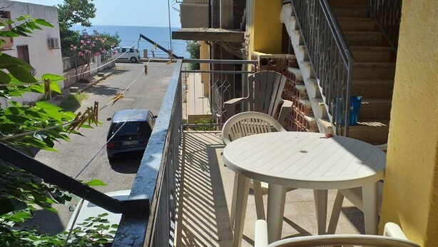 Een balkon met een tafel en stoelen, met uitzicht op een straat met een geparkeerde auto en een gebouw op de achtergrond.