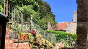 A narrow alleyway with brick walls, potted plants, and a metal gate.