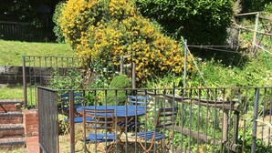 A fenced garden area with a table and chairs, surrounded by various potted plants and a large bush with yellow flowers.