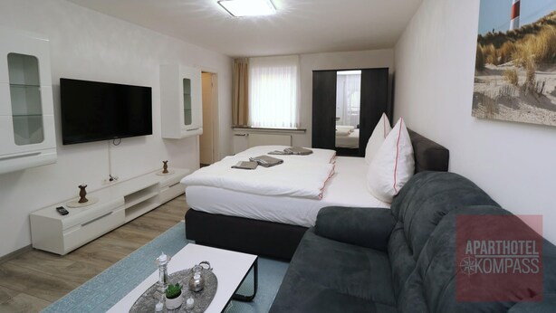 Une chambre d’hôtel moderne équipée d’un lit, d’un canapé, d’une télévision et d’un tableau représentant un phare.
