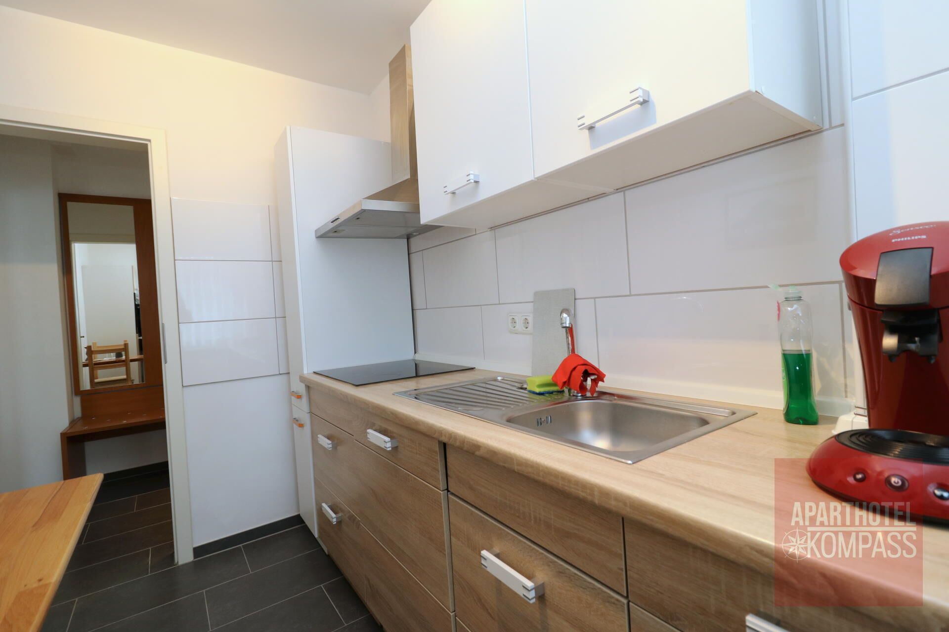 A modern kitchen with white cabinets, a stainless steel sink, and a red coffee machine.