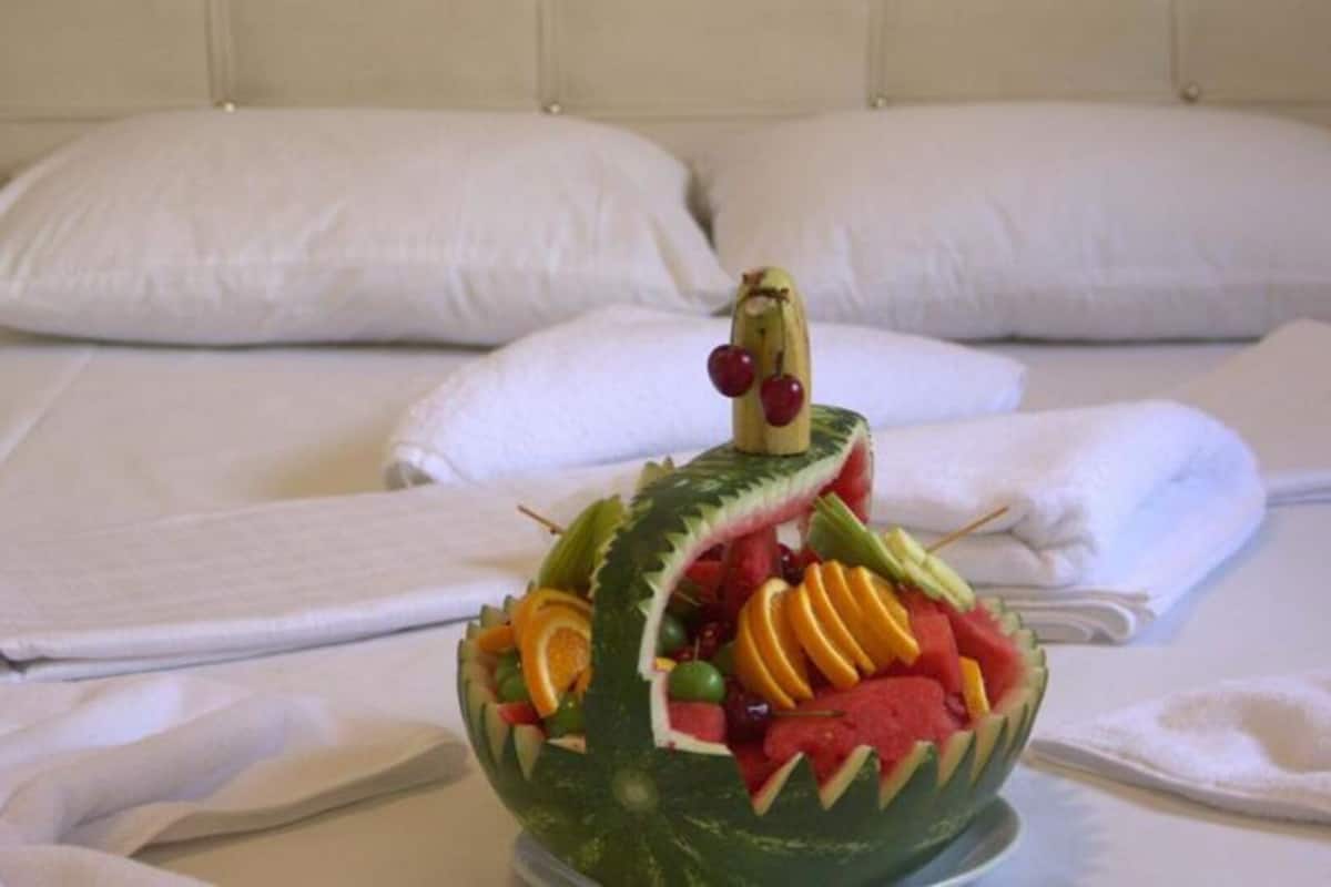 A bed with neatly folded white towels and a fruit arrangement on a tray.