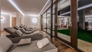 A modern spa room with reclining chairs, a laptop on a table, and a view of a green outdoor area through large glass doors. - Eden Boutique Hotel (Curon Venosta)