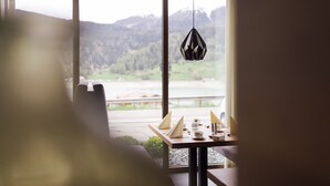 A dining area with a table set for two, a hanging pendant light, and a view of a mountainous landscape through large windows. - Eden Boutique Hotel (Curon Venosta)