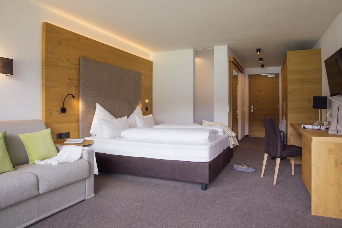 Ein modernes Hotelzimmer mit einem großen Bett, einem Schreibtisch, einem Sessel und einem Fernseher.
