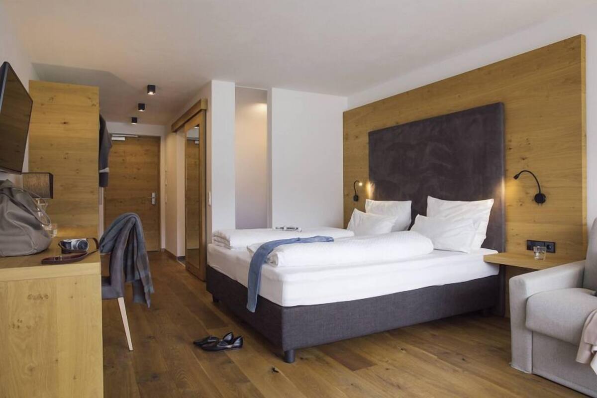 Ein modernes Hotelzimmer mit einem großen Bett, einem Holz-Kopfteil und einem Schreibtisch mit Stuhl.