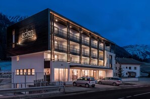 A modern hotel with a prominent 'eden' sign, multiple balconies, and a view of snow-capped mountains.