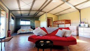 A compact living space with a red sofa, a small kitchen area, and a sleeping area with a bunk bed. - Farmstay cabins in Western Australia, close to highway. (Northampton)