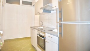 Eine kompakte Küche mit einem Edelstahlkühlschrank, einem eingebauten Backofen und einem Spülbecken.