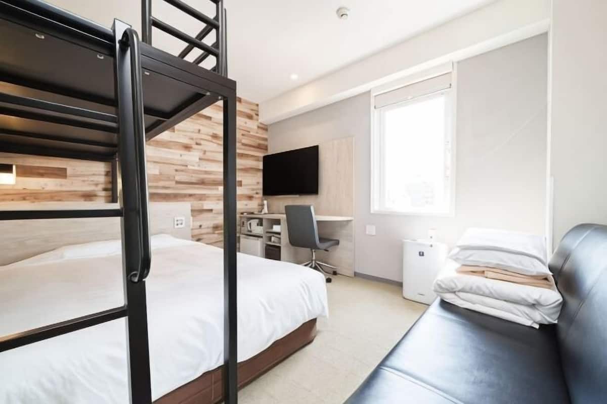 Ein Stockbett, ein Schreibtisch mit Stuhl, ein Fernseher und ein Sofa in einem Zimmer mit Holzwandverkleidung.