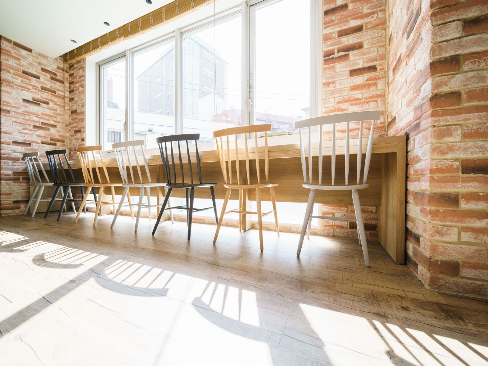 A dining area with six wooden chairs and a table, brick walls, and large windows.