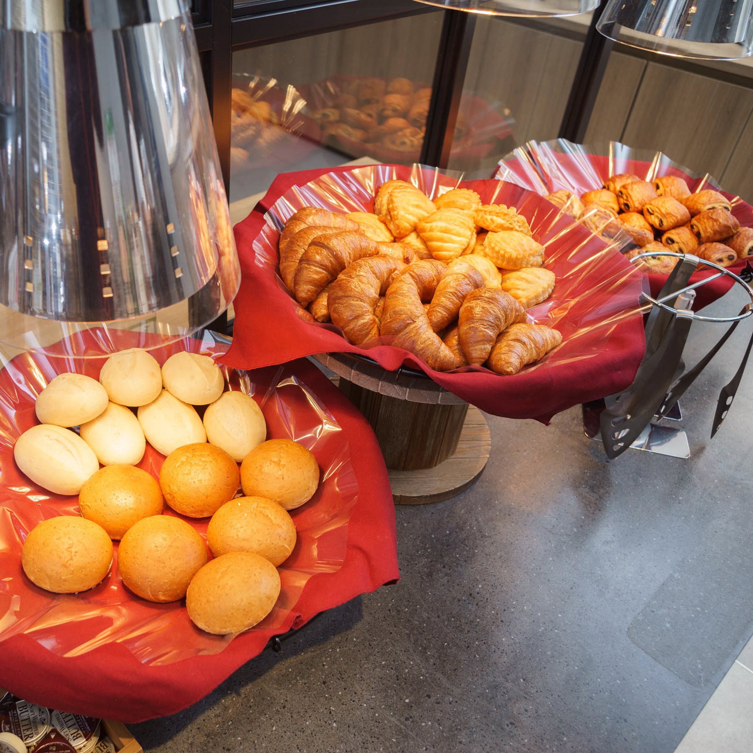 Un bufé con diversas opciones de panadería, incluyendo bollos y pasteles, exhibidos en cestas rojas.
