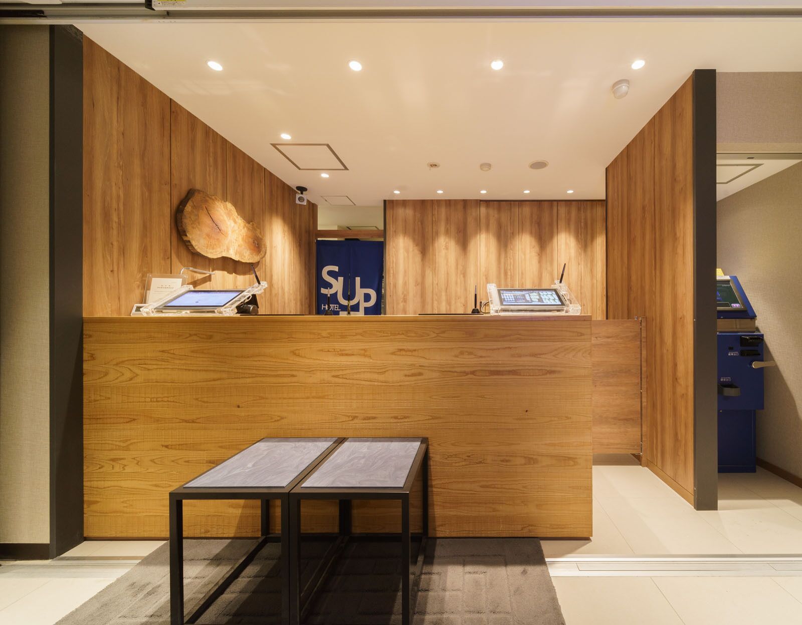 A reception desk with a wooden finish, a digital kiosk, and a blue sign with "SUP" in the background.
