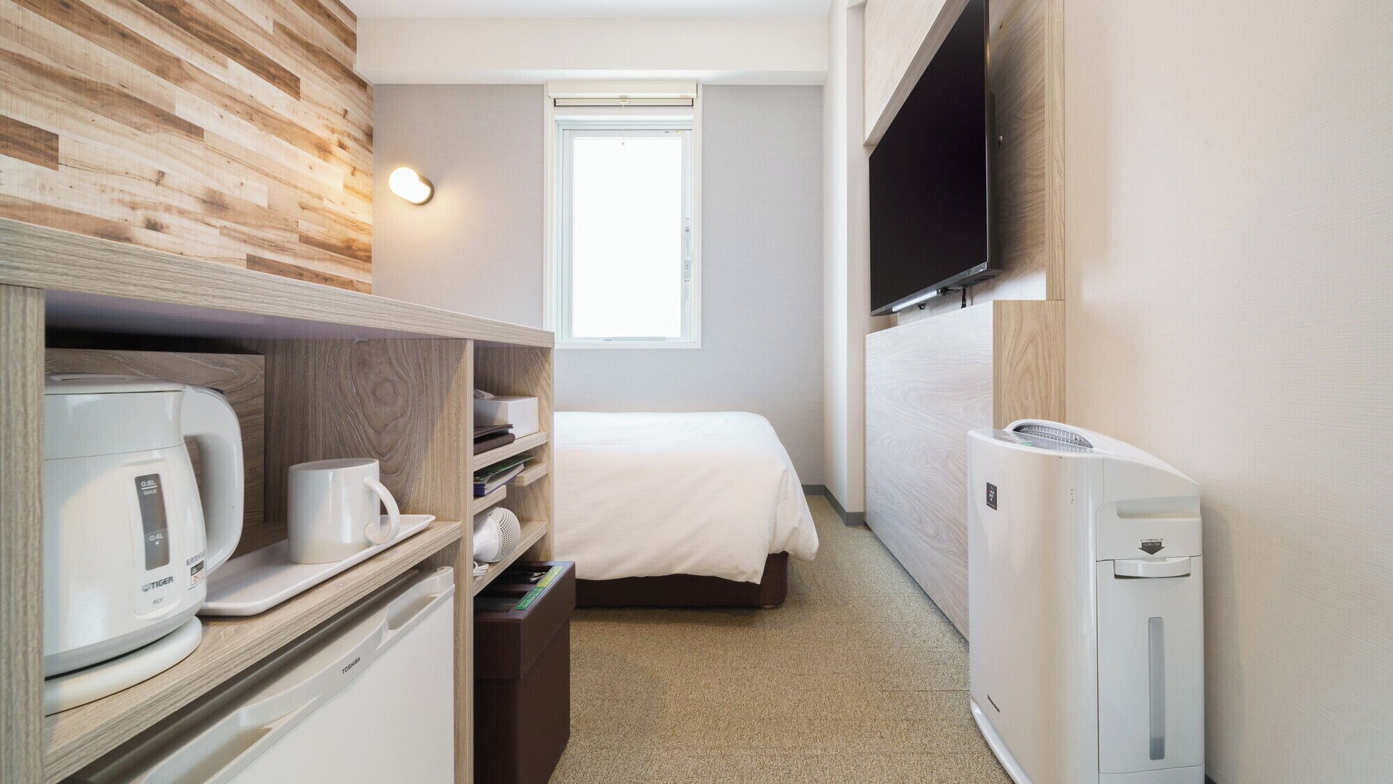 Een kleine hotelkamer met een bed, een aan de muur bevestigde televisie, een koffiezetapparaat en een klein verwarmingselement.