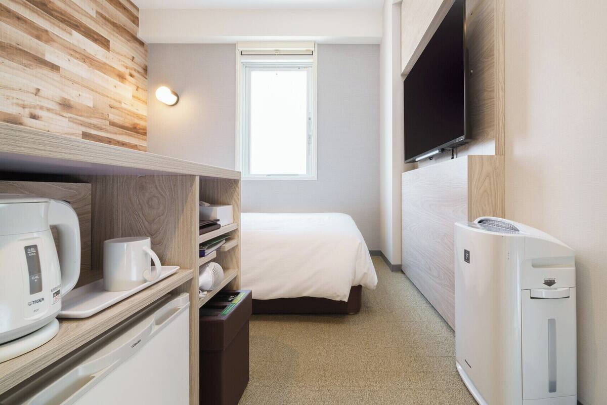 Een kleine hotelkamer met een bed, een aan de muur bevestigde televisie, een koffiezetapparaat en een klein verwarmingselement.
