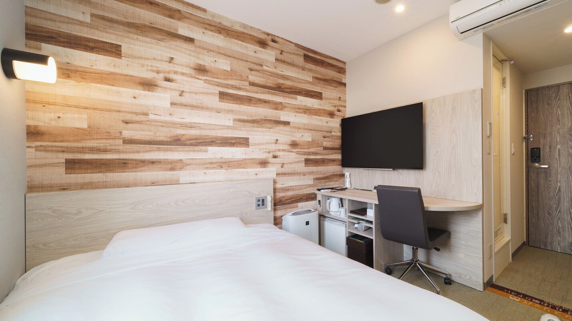 Een hotelkamer met een houten wand, een bed, een bureau met stoel, een televisie en een kitchenette.